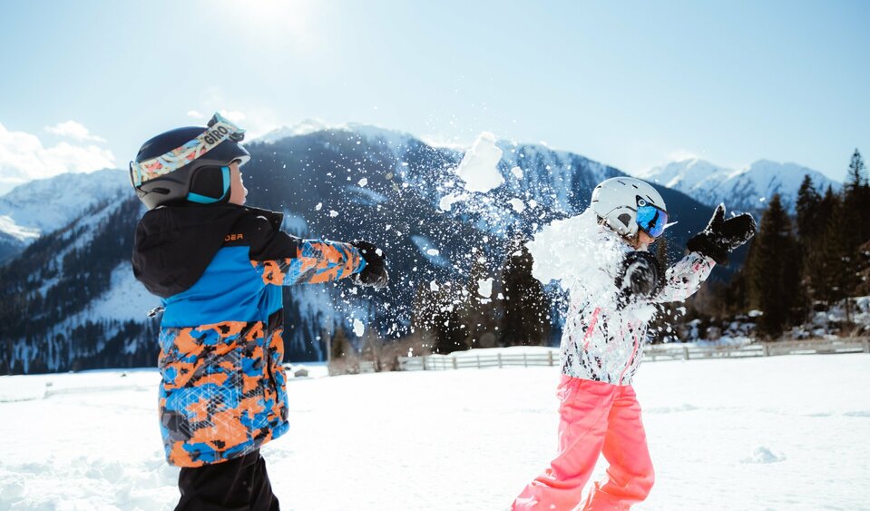 Zwei Kinder machen eine lustige Schneeballschlacht im Kinderland in Obertilliach bei strahlend schönem Wetter.