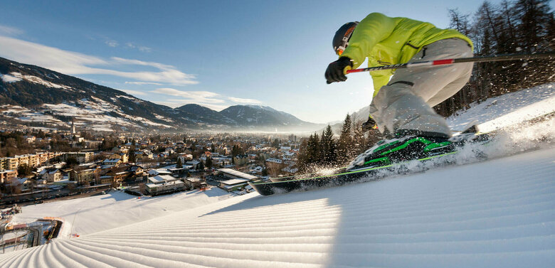 Skifahren Hochstein Ein Skifahrer mit gelber Jacke und heller Hose carved am Hochstein mit den Ski. Aufgenommen von unten. Blick auf das Dorf.