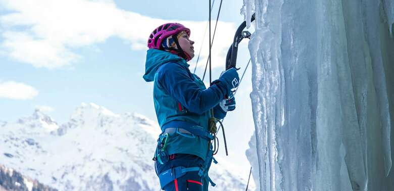 Eine Person steht am Start einer abenteuerlichen Kletterroute über einen zugefrorenen Wasserfall.