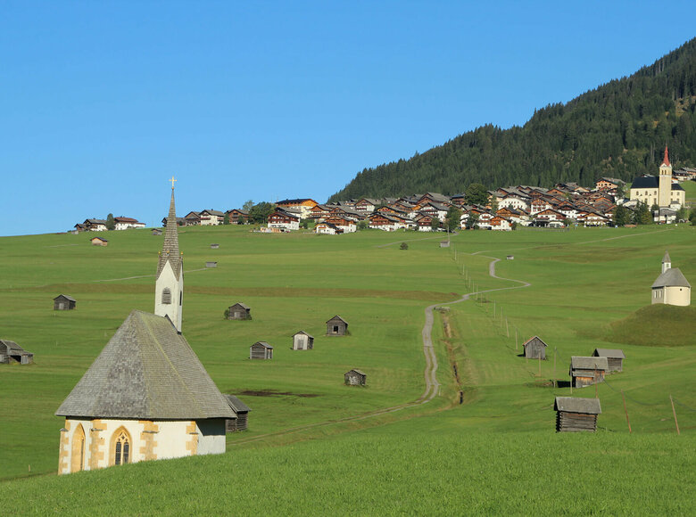 Blick von den Tilliacher Mösern auf das Dorf mit den saftig grünen Wiesen. Zwischen den unzähligen kleinen Heustadeln die 2 Kapellen St. Nikolaus und St. Helena.