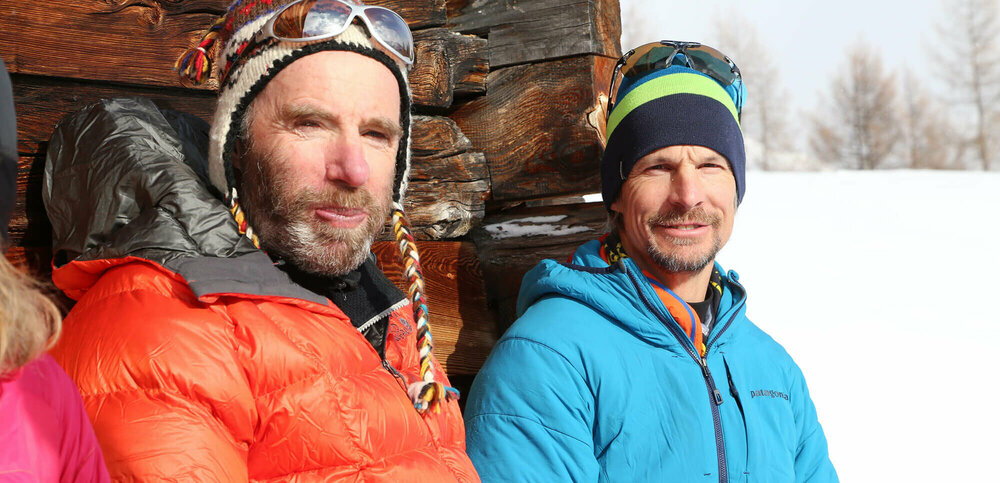 Bergführer Hannes Grüner mit Steve House vor einer kleinen Hütte aus Holz sitzend.
