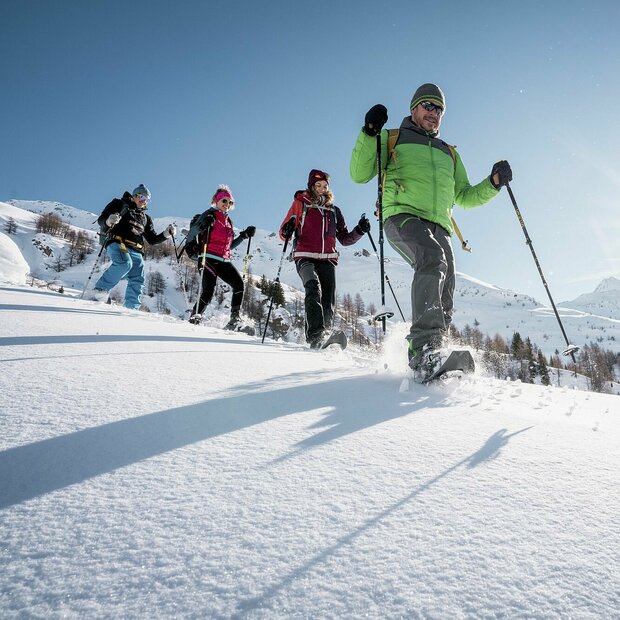 Eine Gruppe mit Ranger beim Schneeschuhwandern in Kals am Großglockner. Die Sonne strahlt im Hintergrund auf die verschneiten Berggipfel.