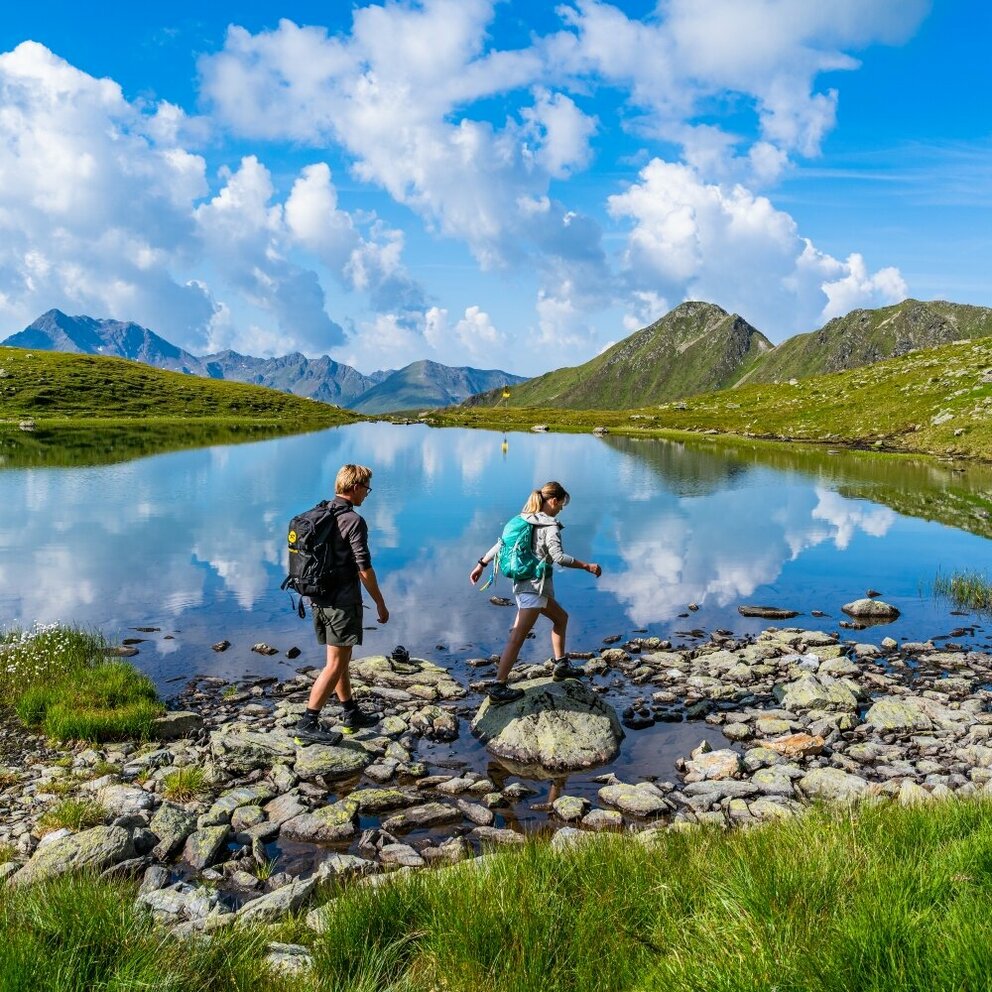 Ein Pärchen steigt über einige Steine am Gritzer See in St.Veit im Defereggen an einem herrlichen Sommertag.