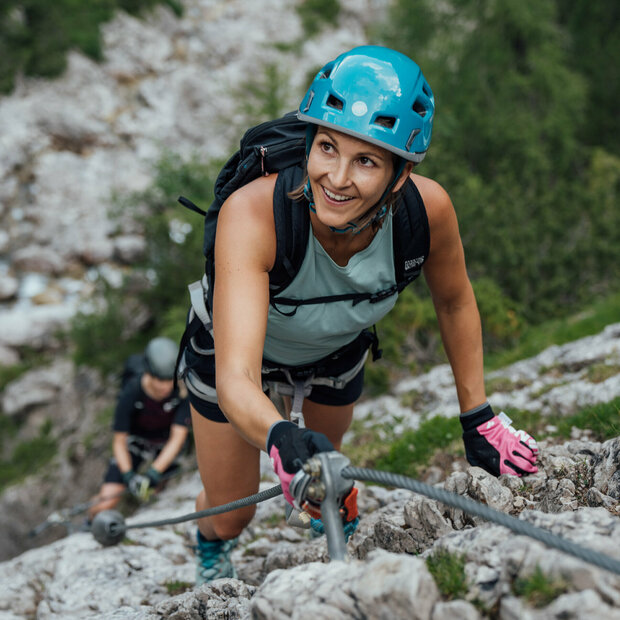 Zwei Frauen klettern am Klettersteig namens "Verborgene Welt" am Fels nach oben.