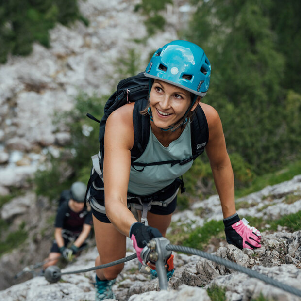 Zwei Frauen klettern am Klettersteig namens "Verborgene Welt" am Fels nach oben.