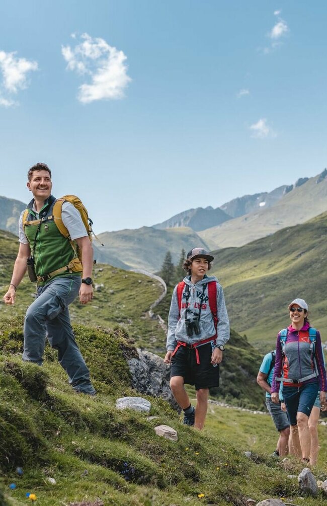 Mehrere Personen wandern durch den Nationalpark Hohe Tauern auf einer Rangertour mit Blick auf die Jagdhausalmen im Hintergrund.