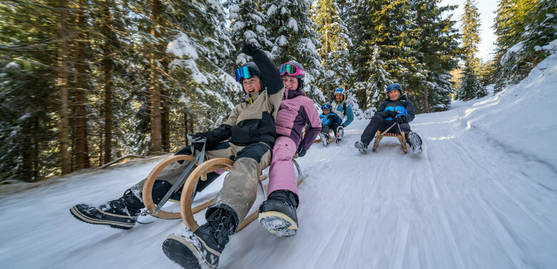 Eine fünfköpfige Familie in bunten Skianzügen auf der rasanten Rodelabfahrt in Außervillgraten.