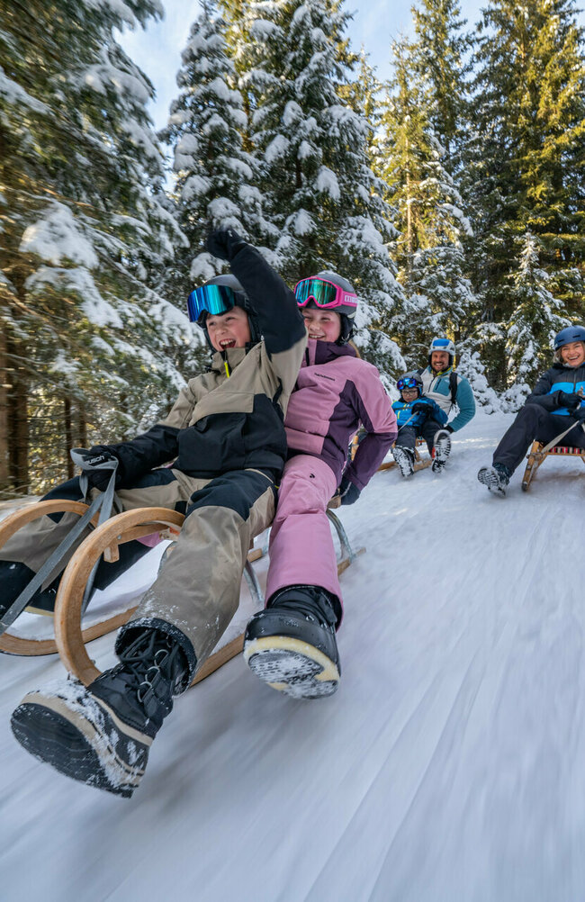 Eine fünfköpfige Familie in bunten Skianzügen auf der rasanten Rodelabfahrt in Außervillgraten.