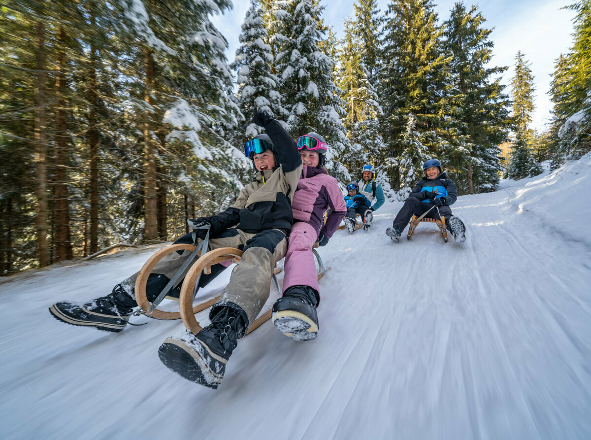 Eine fünfköpfige Familie in bunten Skianzügen auf der rasanten Rodelabfahrt in Außervillgraten.