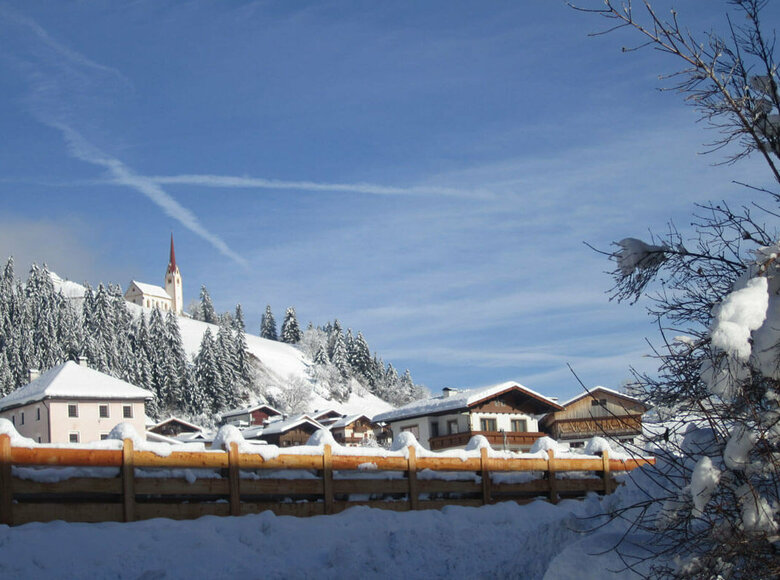 Blick auf Strassen mit der Kirche auf einer Anhöhe im Winter bei strahlend blauem Himmel und Schnee.