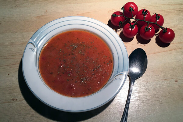 Ein Teller mit Tomatensuppe und einem Löffel und mehreren Kirschtomaten daneben.