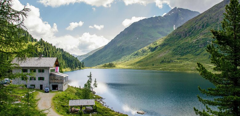 Ruhiger Blick über den Obersee am Staller Sattel, rechts am Ufer eingebettet zwischen Lärchen und Zirben liegt das Gasthaus Obersee