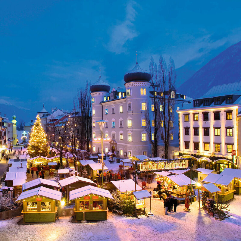 Aufnahme vom Lienzer Adventmarkt am Hauptplatz bei Nacht. Die Hütten und ein großer Tannenbaum in der Mitte sind beleuchtet.