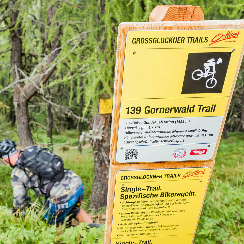 Mountainbiker bei einem Hinweisschild betreffend der Verhaltensreglen beim Biken