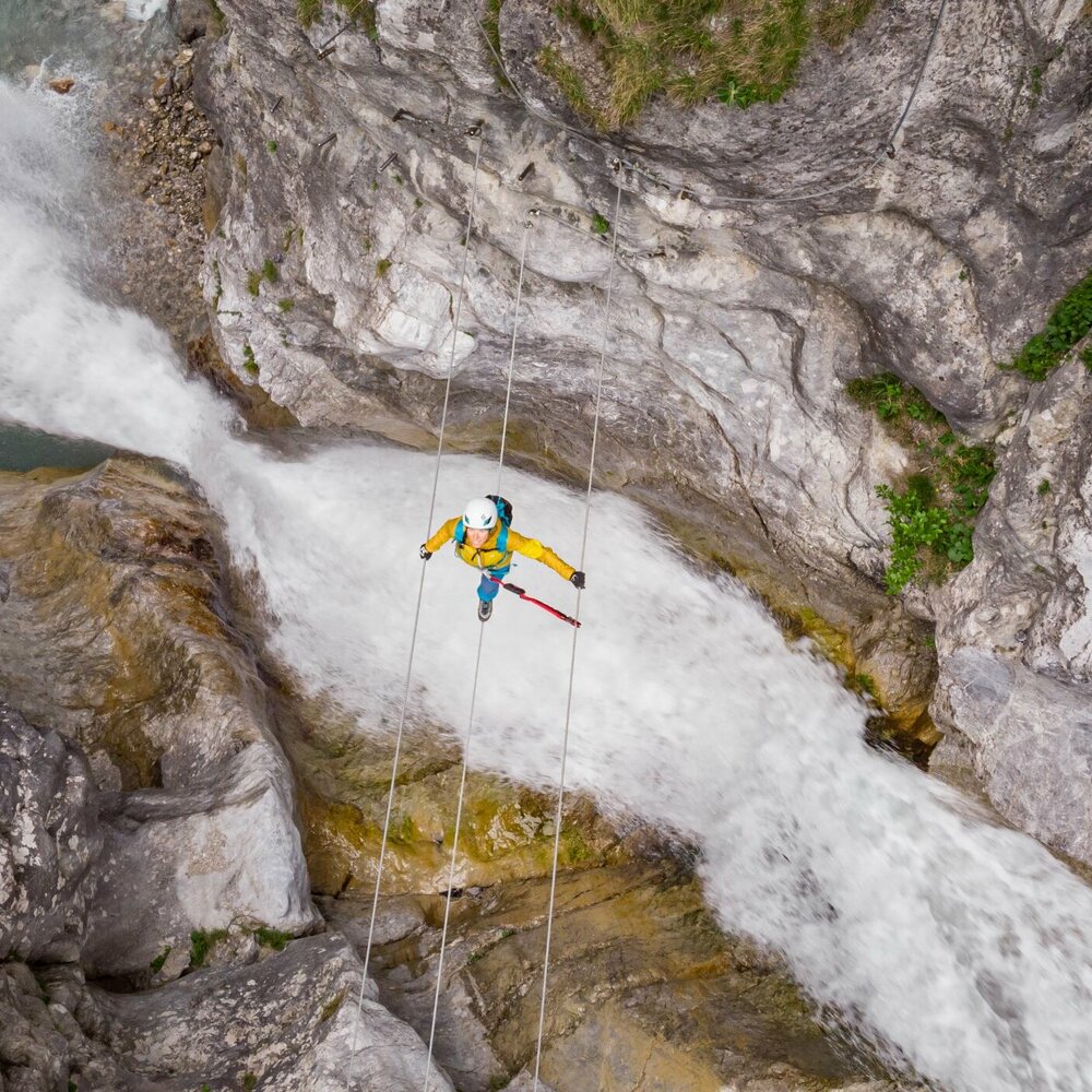Eine Frau mit gelber Jacke geht über eine luftige Seilbrücke über den Fluss in der Galitzenklamm.