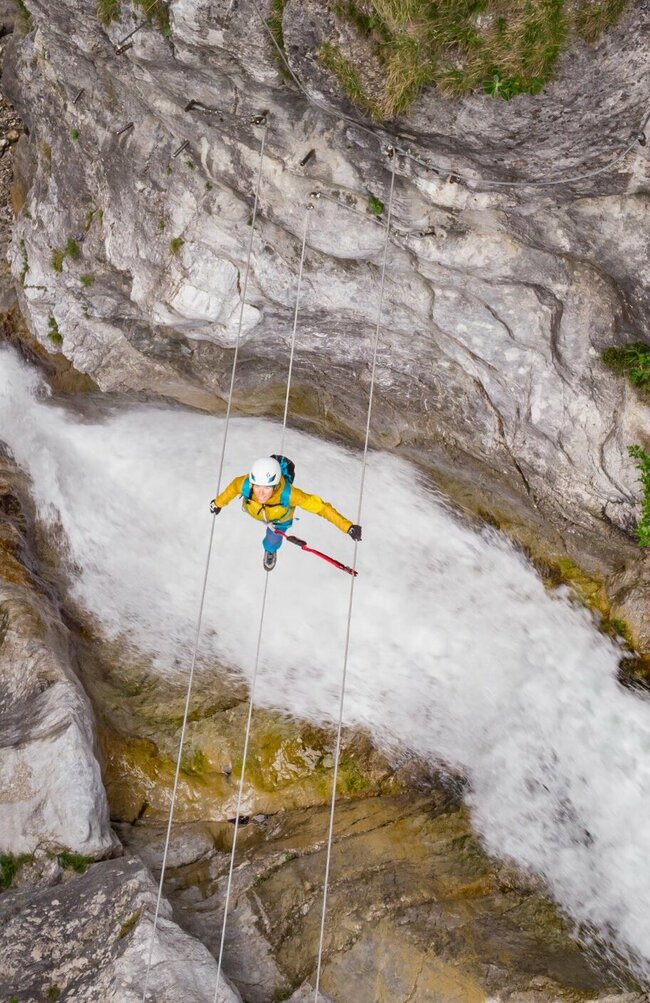 Eine Frau mit gelber Jacke geht über eine luftige Seilbrücke über den Fluss in der Galitzenklamm.