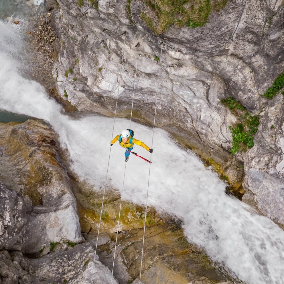 Eine Frau mit gelber Jacke geht über eine luftige Seilbrücke über den Fluss in der Galitzenklamm.