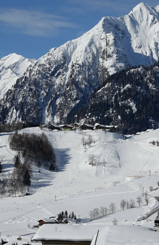 Blick von oben auf das Familienskigebiet Prägraten am Großvenediger mit schneebedeckter Bergkulisse im Hintergrund.