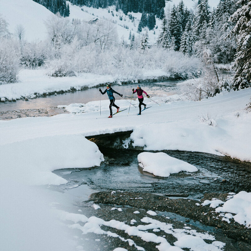Zwei Langläufer:innen laufen am Gewässer vorbei in Innervillgraten