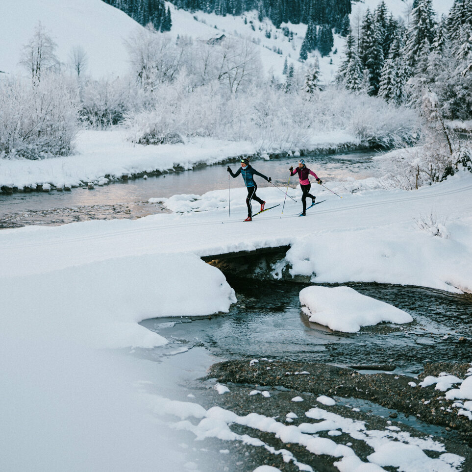 Zwei Langläufer:innen laufen am Gewässer vorbei in Innervillgraten