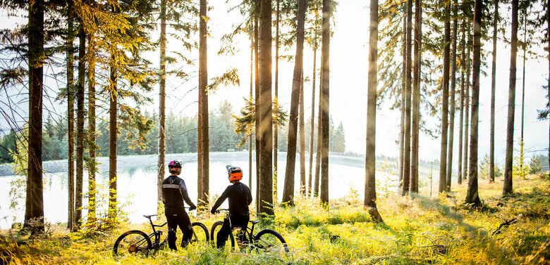 Bikepark Lienz Zwei Radfahrer stehen im Wald im Bikepark Lienz, während die Sonne durch die Bäume blitzt.