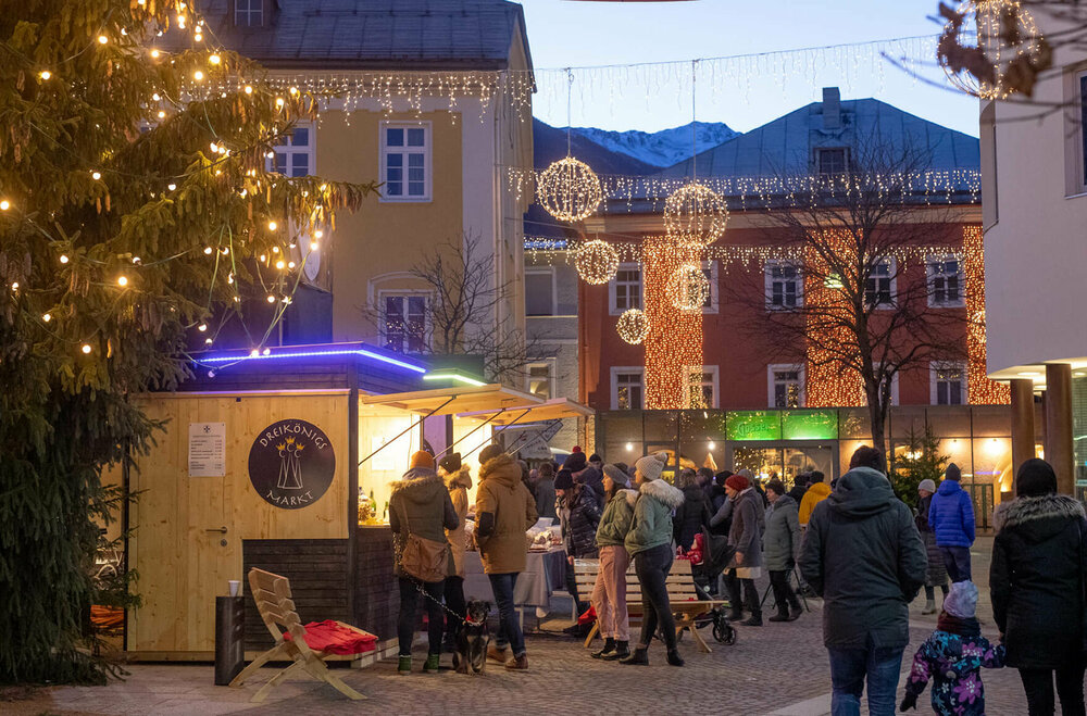 Menschen beim Dreikönigsmarkt am Lienzer Hauptplatz in der Abenddämmerung.