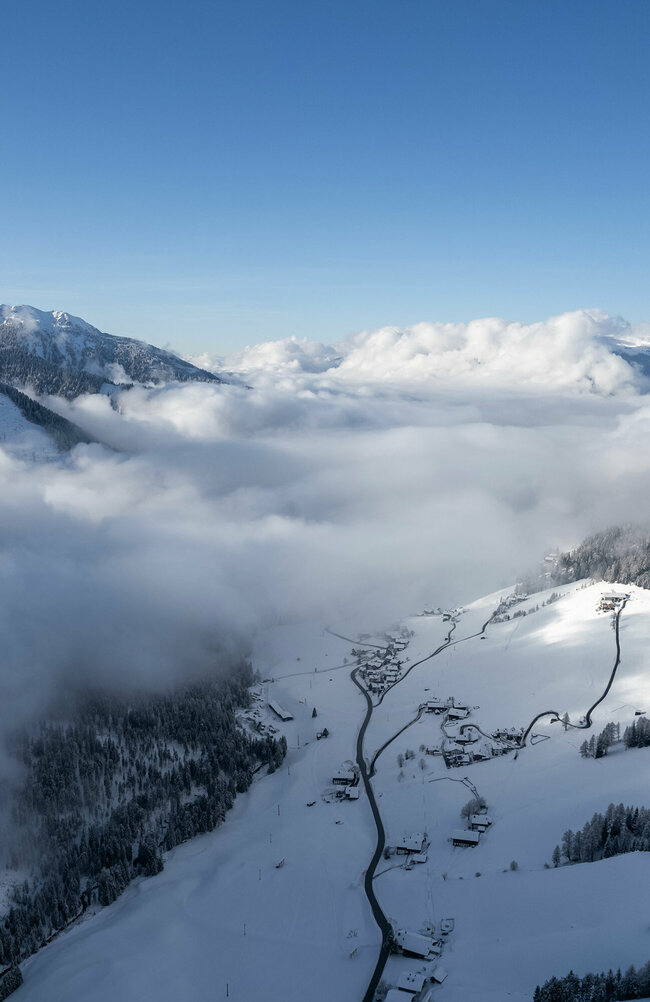 Luftaufnahme des Tiroler Gail- und Lesachtales bei herrlicher Winterstimmung mit leichten Nebelschwaden und frisch verschneiten Wäldern.