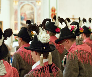 Mehrere Personen in Tracht mit schwarzen Hüten und Blumen am Schutzengelsonntag.