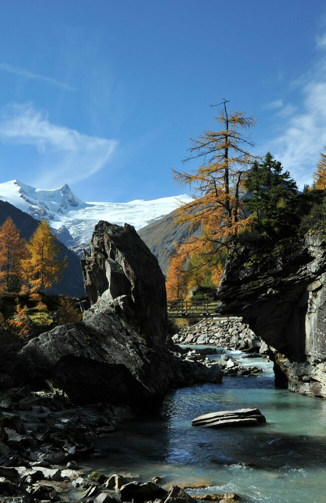 Der Tauernbach im Herbst mit Blick auf das schneebedeckte Schlatenkees im Hintergrund.