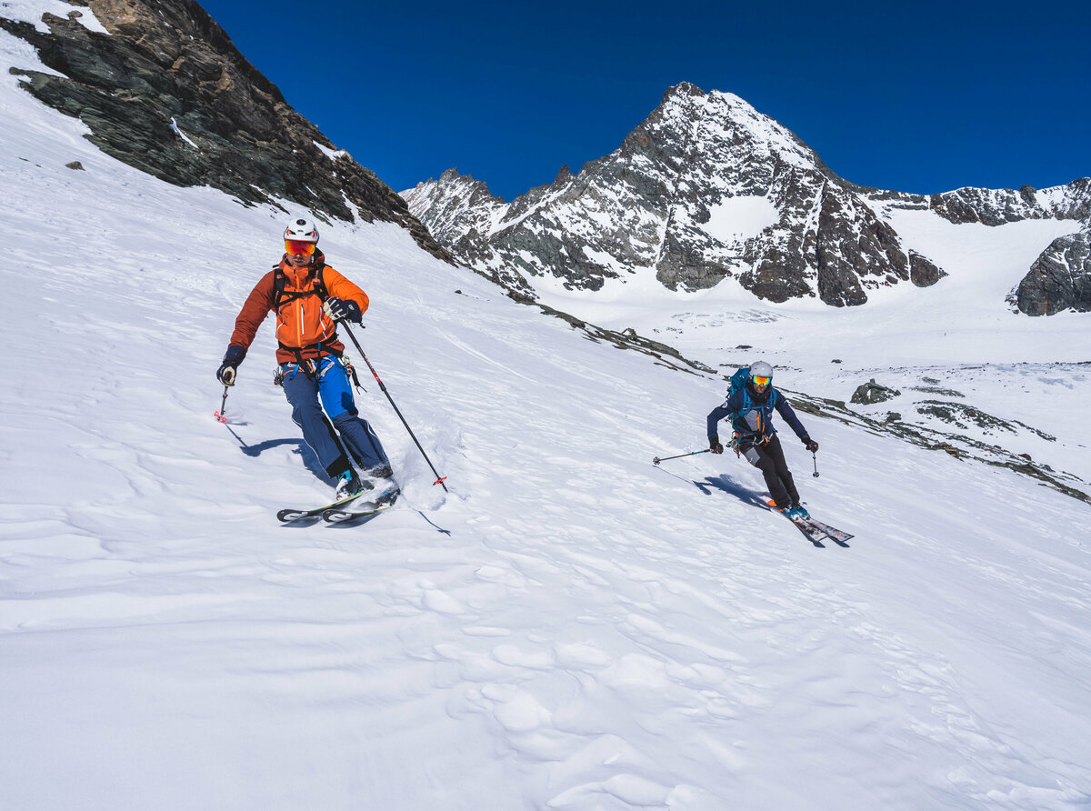 Zwei Skifahrer:innen bei der Abfahrt mit Großglockner im Hintergrund