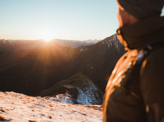 Wanderer betrachtet am Figerhorn, wie die Sonne langsam hinter den umliegenden Bergen untergeht.