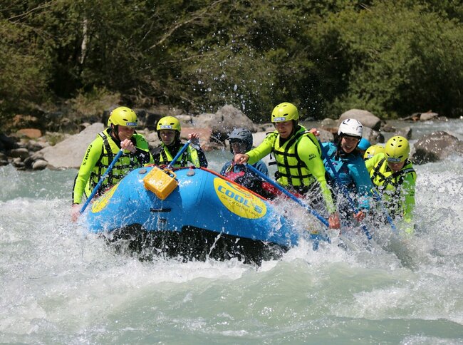 Rafting in summer A group of people while water rafting on a river. They are sitting together in a blue inflatable boat. They are wearing protective clothing such as helmets and life jackets in eye-catching colors.
