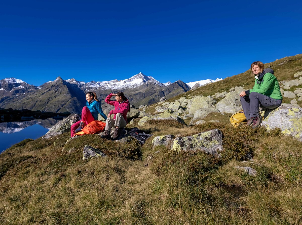 Drei Frauen sitzen auf Felsen am Rande eines Sees im Nationalpark Hohe Tauern während einer Rangertour.