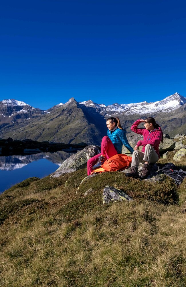 Drei Frauen sitzen auf Felsen am Rande eines Sees im Nationalpark Hohe Tauern während einer Rangertour.