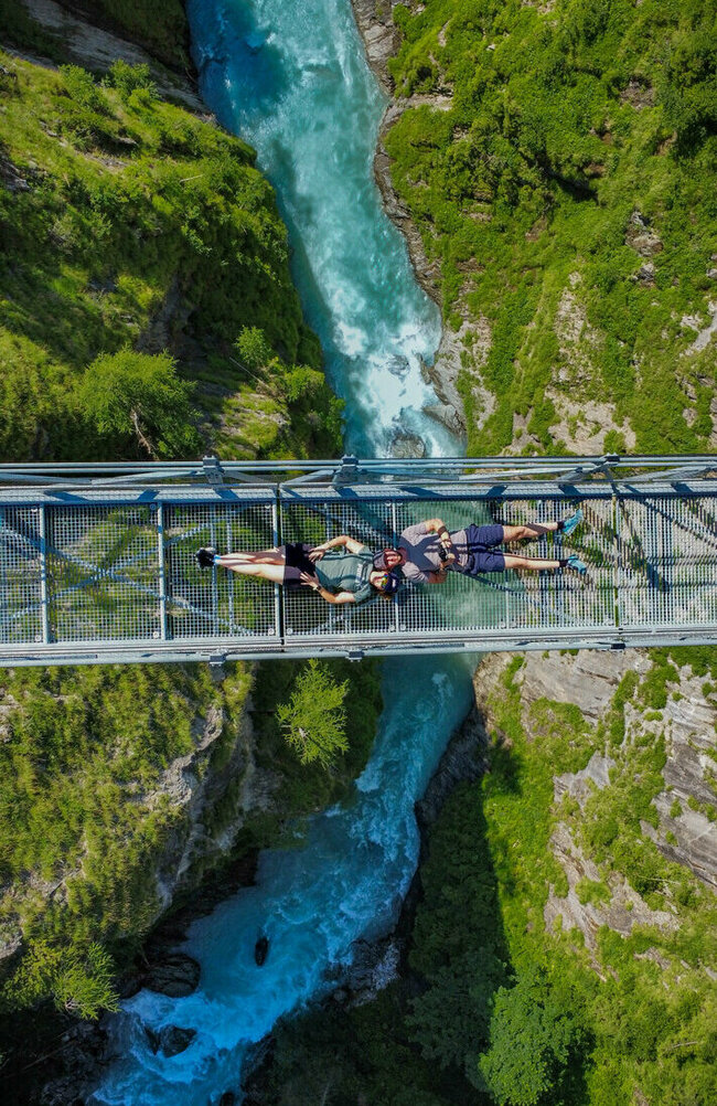 Die Iseltrail-Hängebrücke aus der Vogelperspektive mit zwei Menschen, die darauf liegen und der blauen Isel tief darunter.