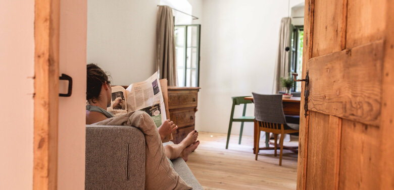 Eine Frau entspannt in ihrer Unterkunft auf einem Sofa und liest Zeitung.