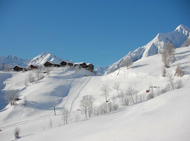 Das schneebedeckte Skigebiet Bichllift. Blick auf einen Skilift und mehrere Gebäude auf einem Hügel.