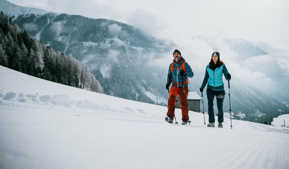 Ein Pärchen wandert auf perfekt präparierten Winterwanderwegen durch Osttirols Winterlandschaft.