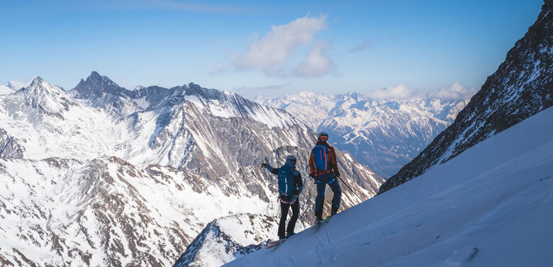 Zwei Skitourengeher:innen genießen den Ausblick aufs Regentörl und blicken in die verschneite Berglandschaft.