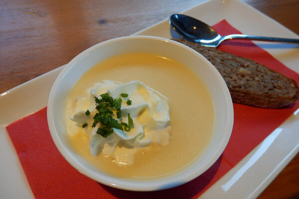 Eine Portion Käserahmsuppe mit Schlag und einer Scheibe dunklem Brot daneben.