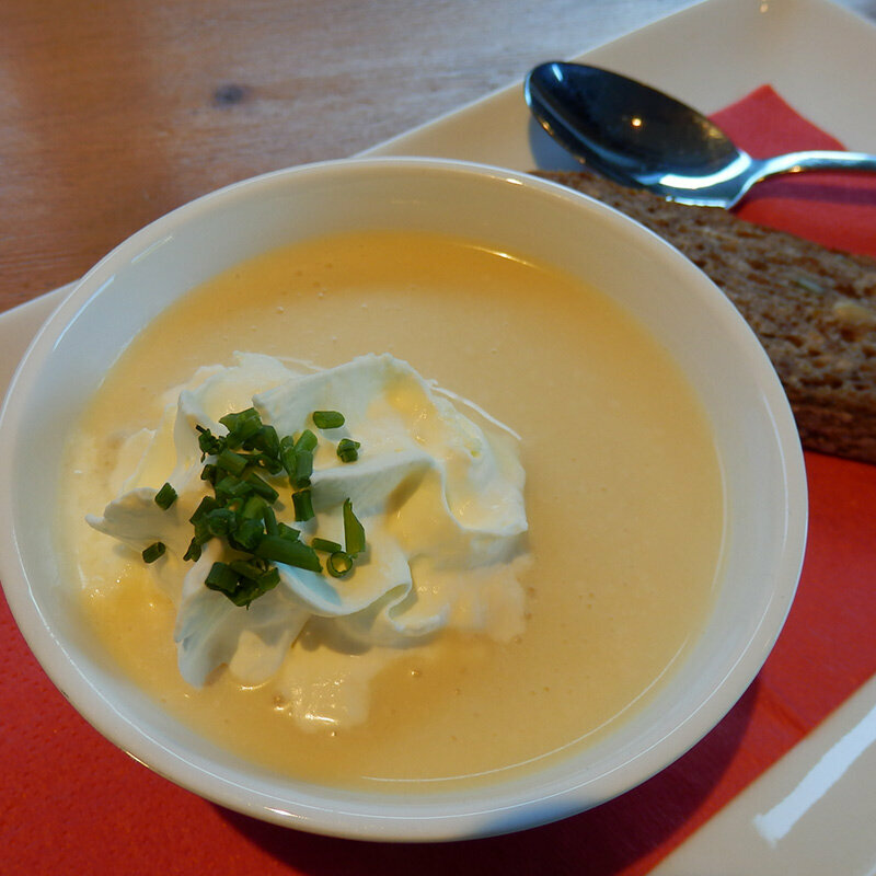 Eine Portion Käserahmsuppe mit Schlag und einer Scheibe dunklem Brot daneben.