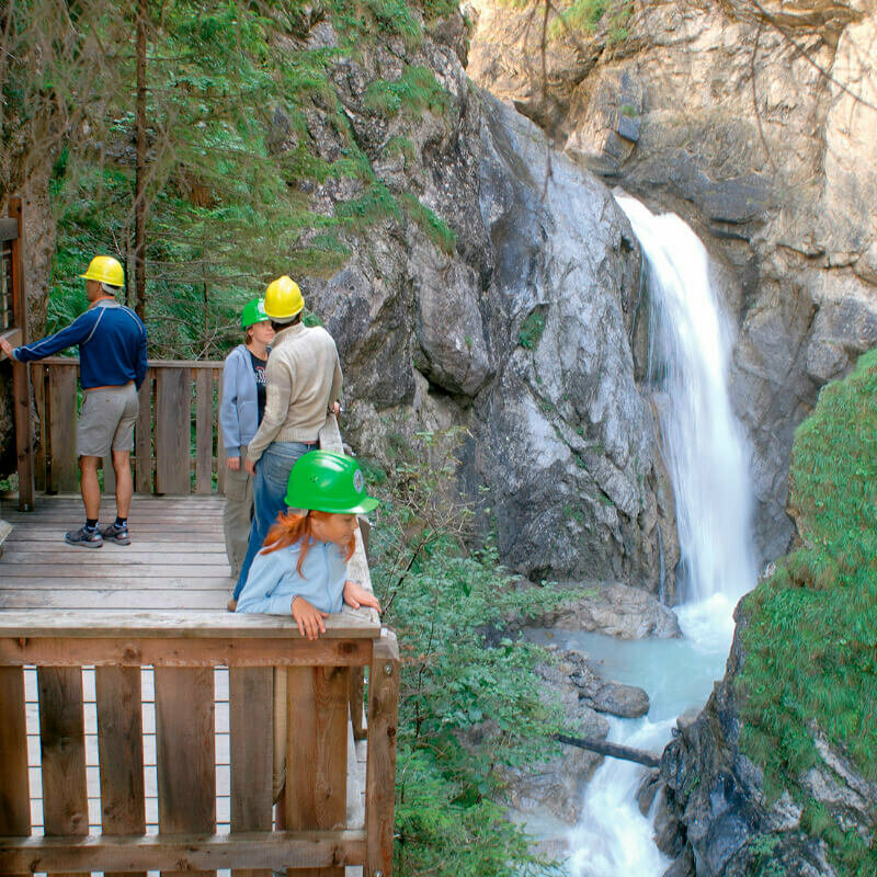 Vier Personen stehen fasziniert auf der Aussichtskanzel des Wasserschaupfades und beobachten das tosend herabschießende Wasser in der Schlucht.