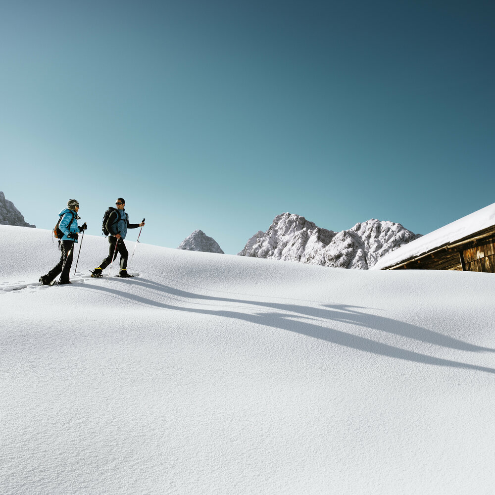 Schneeschuhwandern Zwei Personen wandern mit den Schneeschuhen bei schönem Winterwetter durch den Pulverschnee zu einer Hütte.