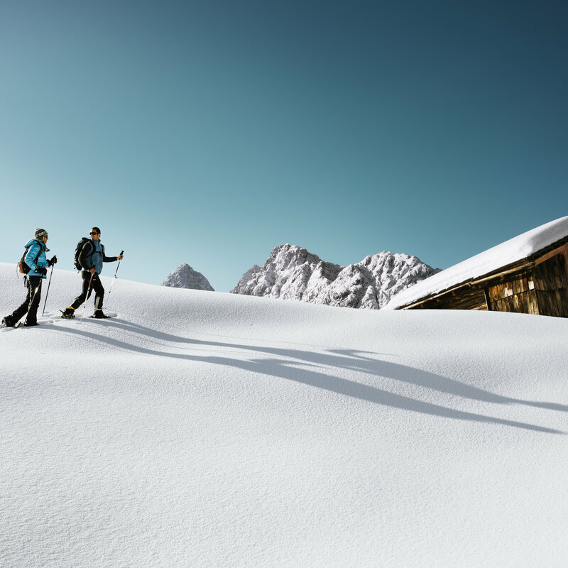 Schneeschuhwandern Zwei Personen wandern mit den Schneeschuhen bei schönem Winterwetter durch den Pulverschnee zu einer Hütte.
