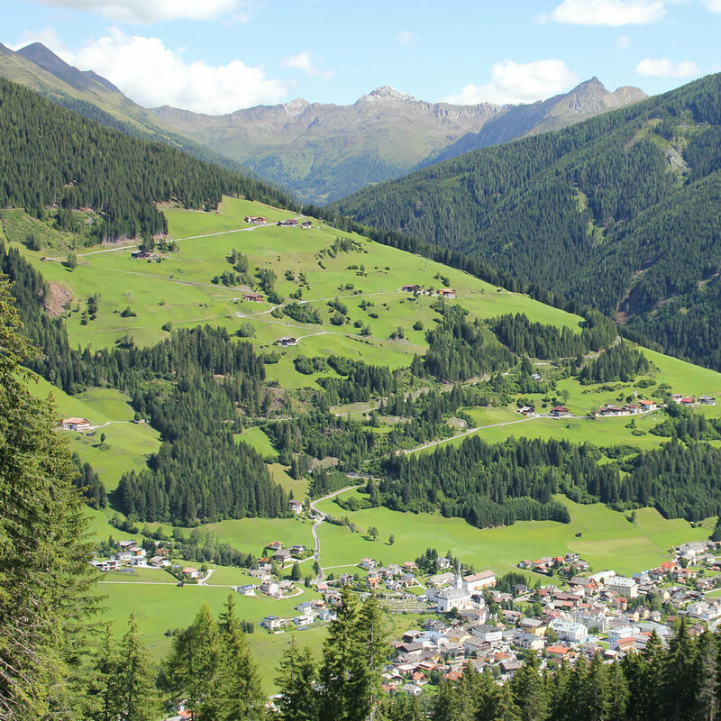 Ortsansicht aus der Ferne auf Sillian mit dem Weiler Sillianberg im Sommer umgeben von grünen Wiesen und Wäldern.