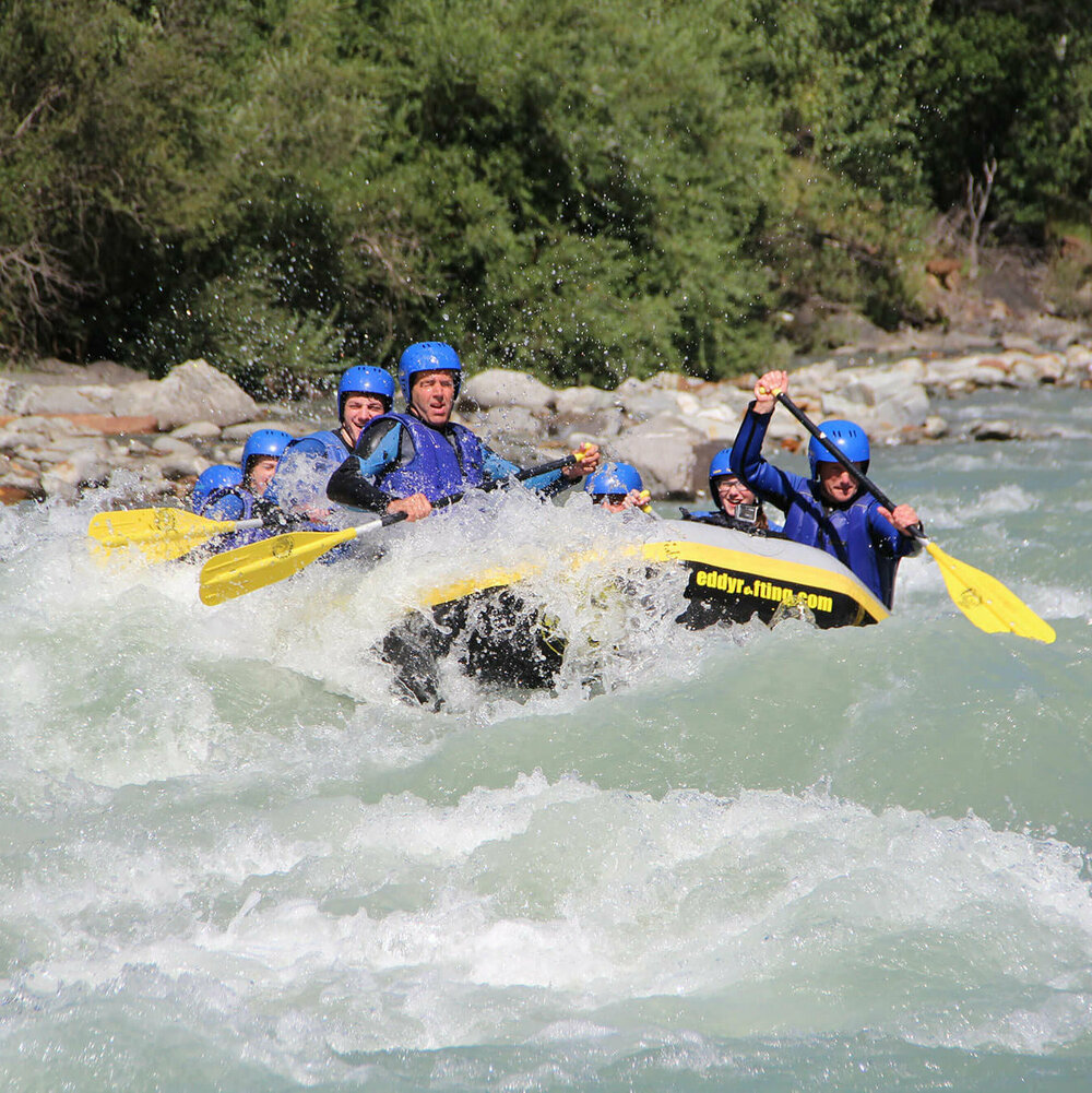 Mehrere Personen in blauen Anzügen und Helmen sitzen in einem gelb-schwarzen Schlauchboot und sind am Raften in Osttirol.