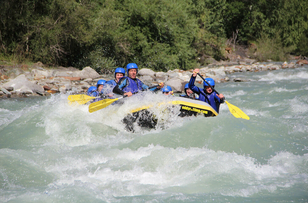 Raften in Osttirol Mehrere Personen in blauen Anzügen und Helmen sitzen in einem gelb-schwarzen Schlauchboot und sind am Raften in Osttirol.