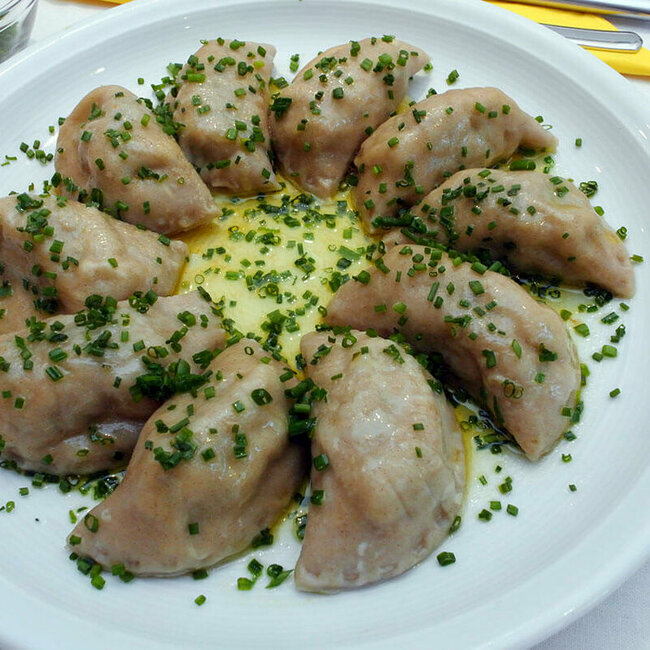 Osttiroler Schlipfkrapfen mit Schnittlauch und geschmolzener Butter auf einem weißen Teller angerichtet.