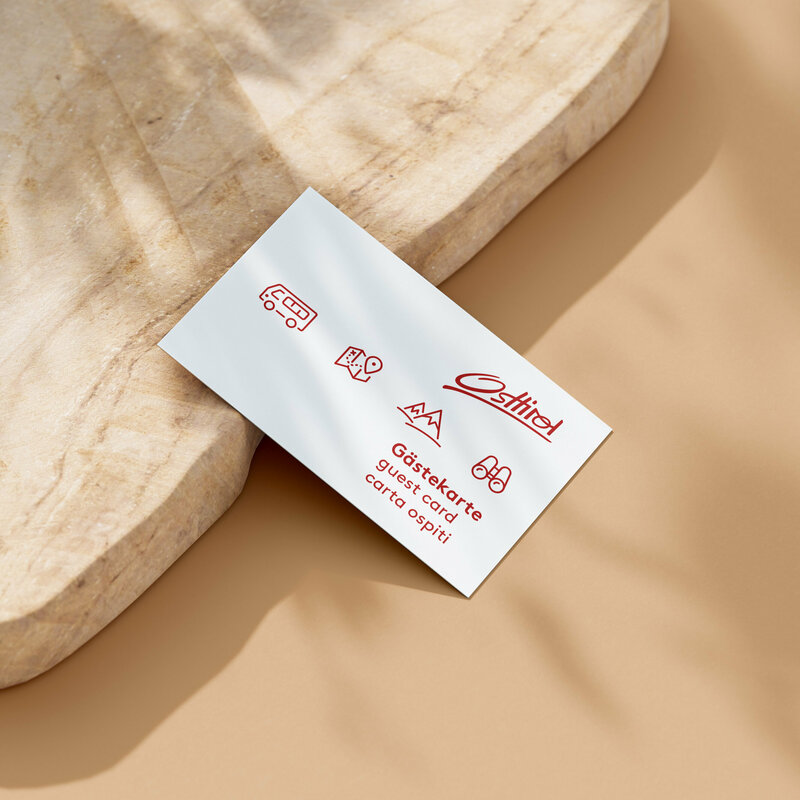 Die Osttiroler Gästecard mit roter Schrift auf weißem Papier, dahinter Holz.