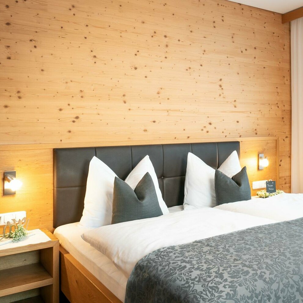 Doppelbett mit Bettbezug in weiß und grau und hölzernes Getäfel auf der Wand